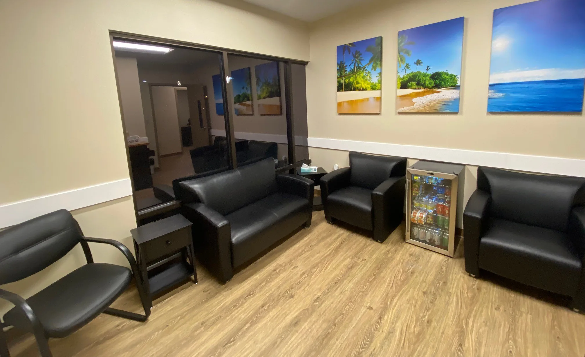 Seating area with black leather sofa and chairs, beach artwork and a drinks fridge at Freedom Detox