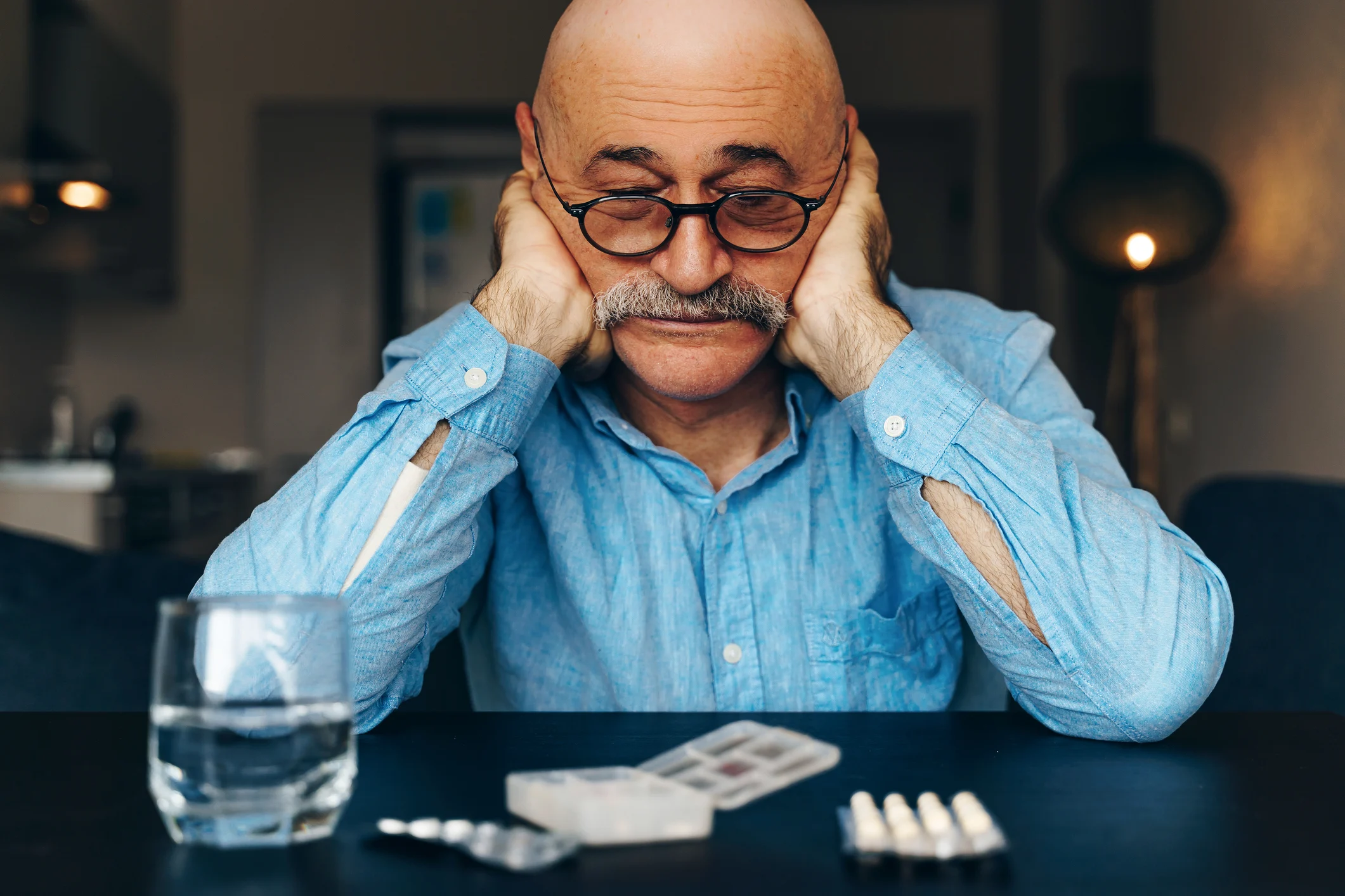 Man sitting with head resting in hands staring at pills on table in front of him