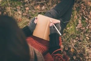 Woman sitting on the ground writing in her notebook