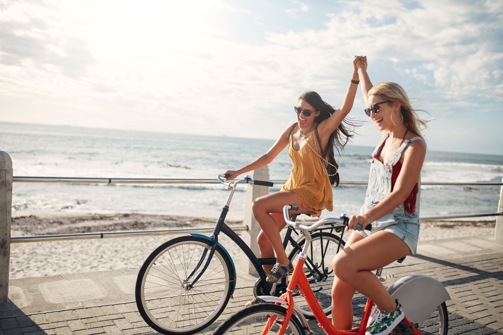 Two girls that are friends riding their bikes along the shore and holding hands