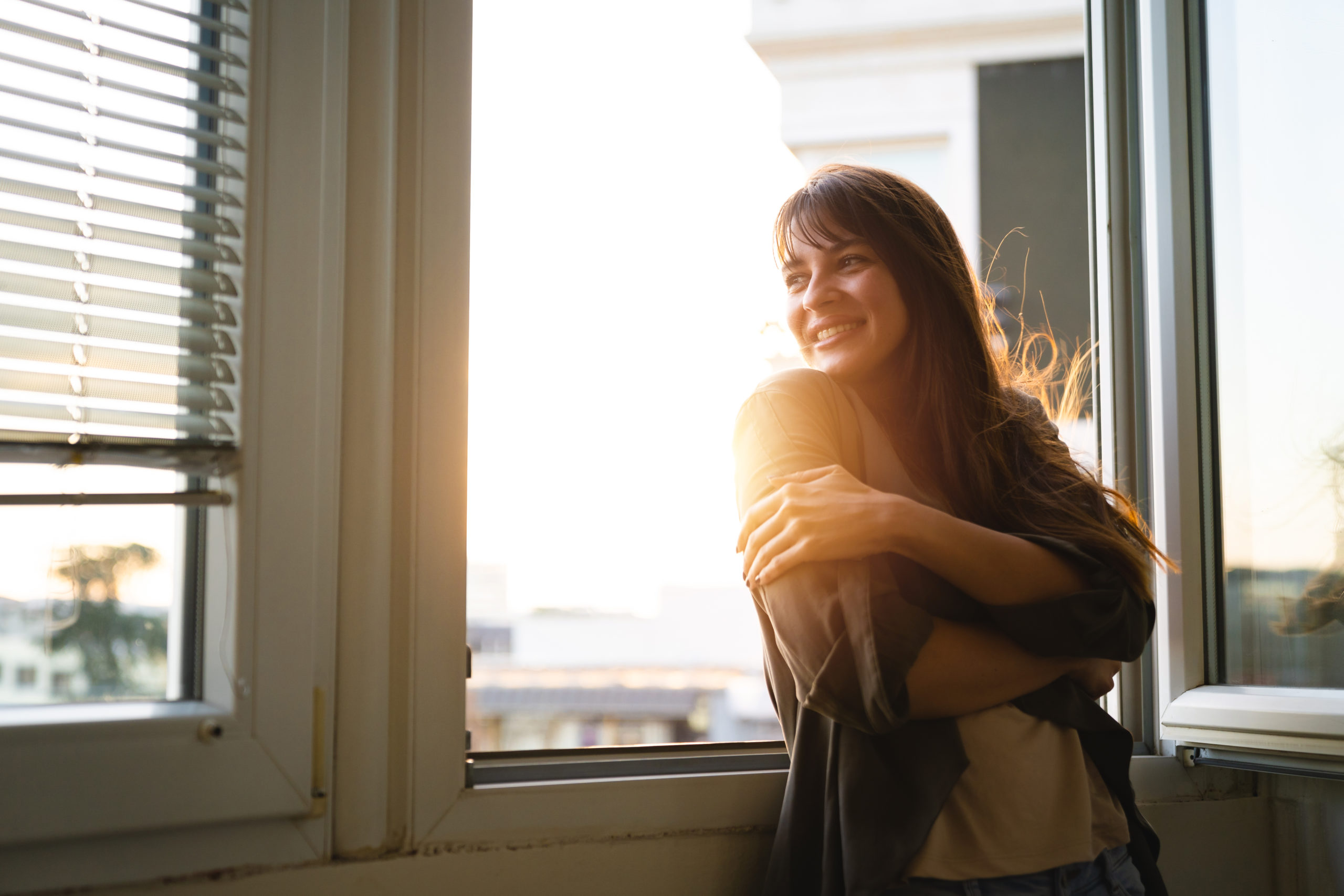 Beautiful young woman looking through the window while enjoying fresh air