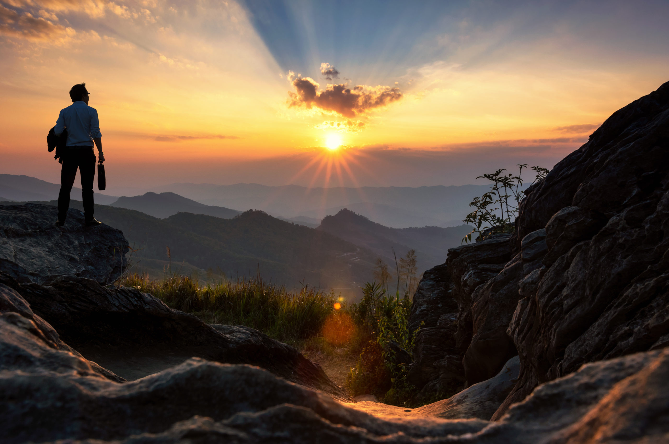 Concept vision, Young businessman wearing comfortable casual suit jacket standing holding a work bag on top of peak mountain and looking forwards, success, competition and leader concept.