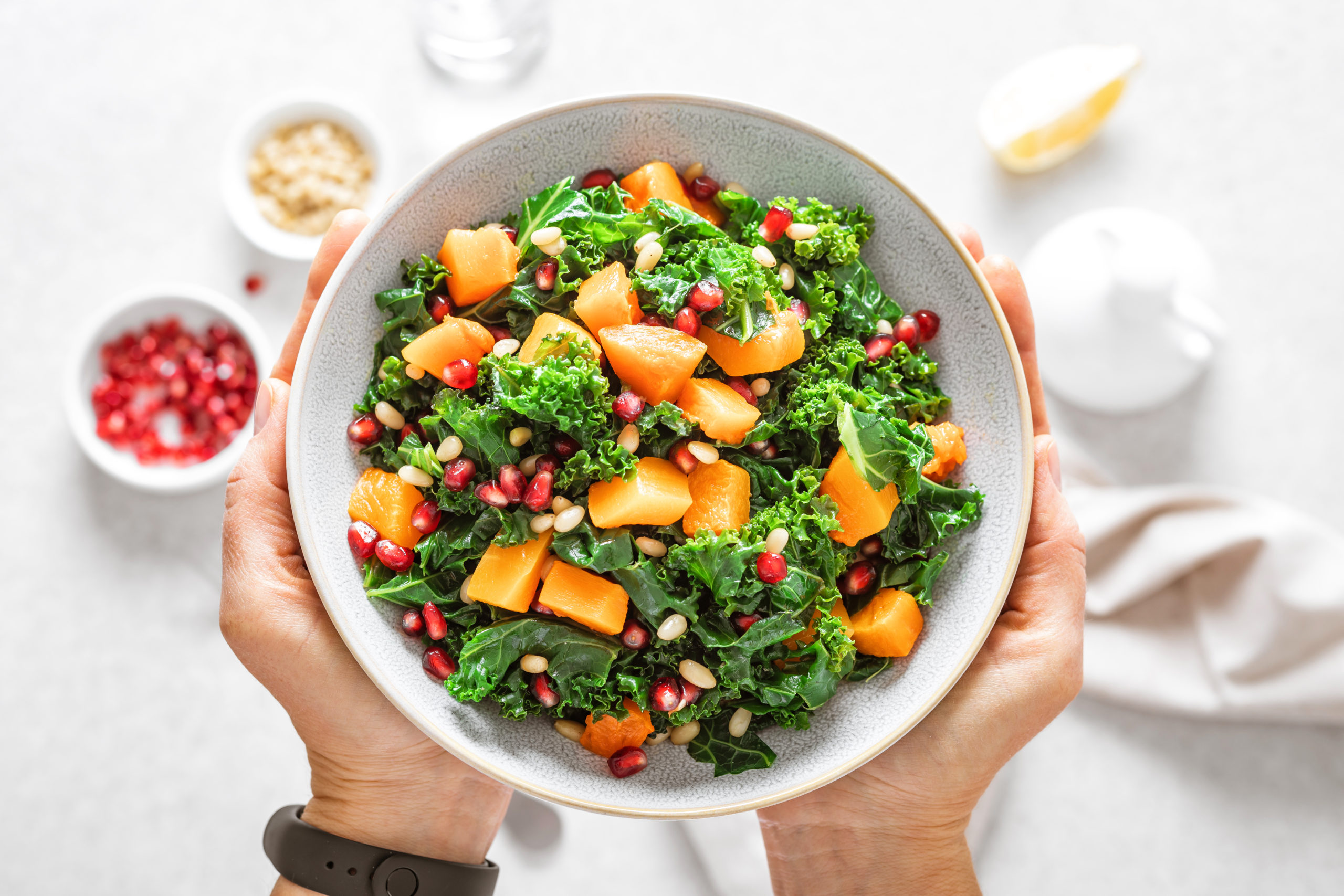 Vegetable salad bowl in woman hands. Fresh kale and baked pumpkin salad. Healthy eating concept