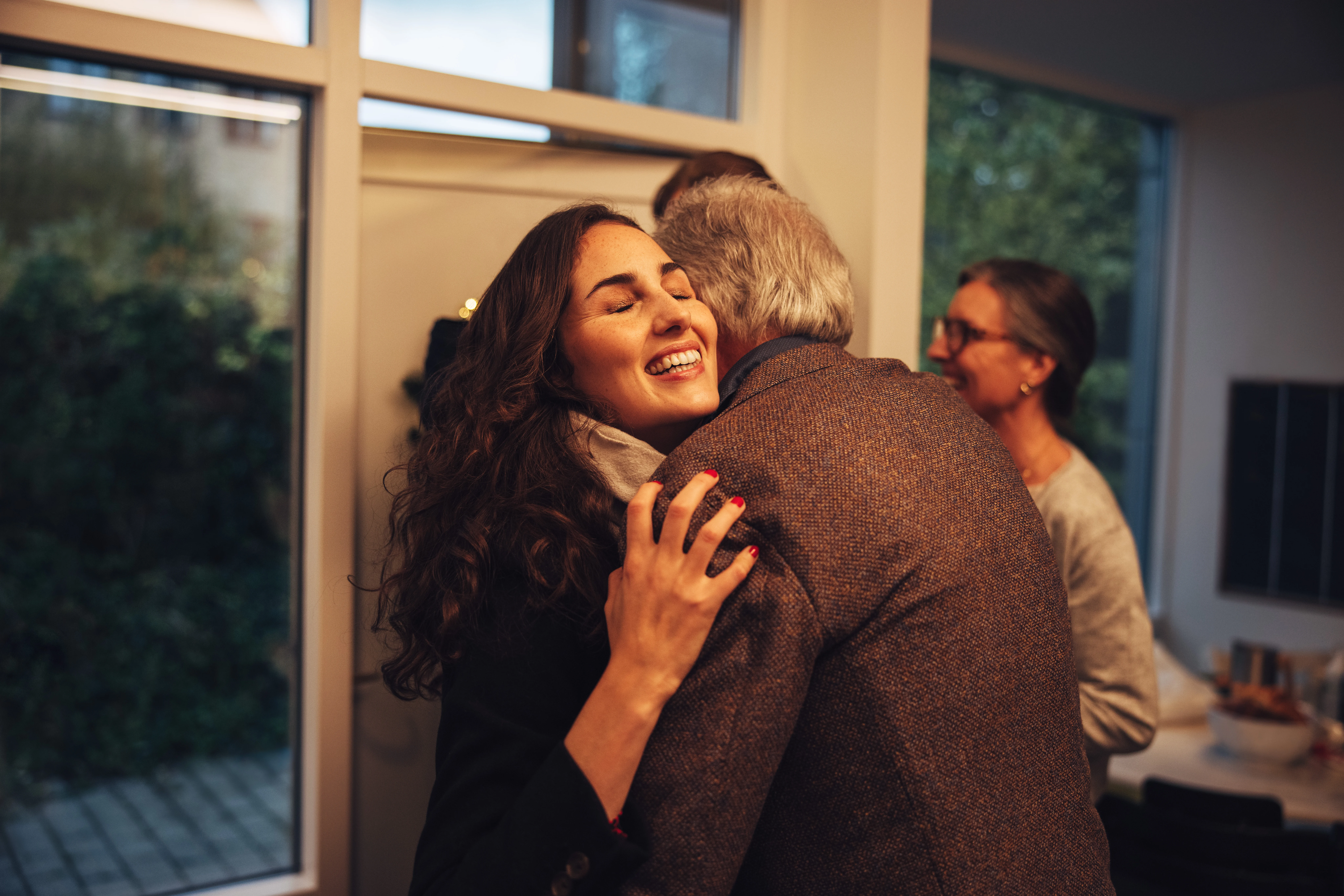 Grandparents greeting and welcoming visiting family at front door. Family coming over for Christmas dinner at the grandparents home.