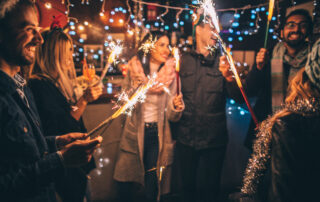 Photo of a cheerful group of friends, at an outdoor New Year's celebration, lightning sparklers at midnight