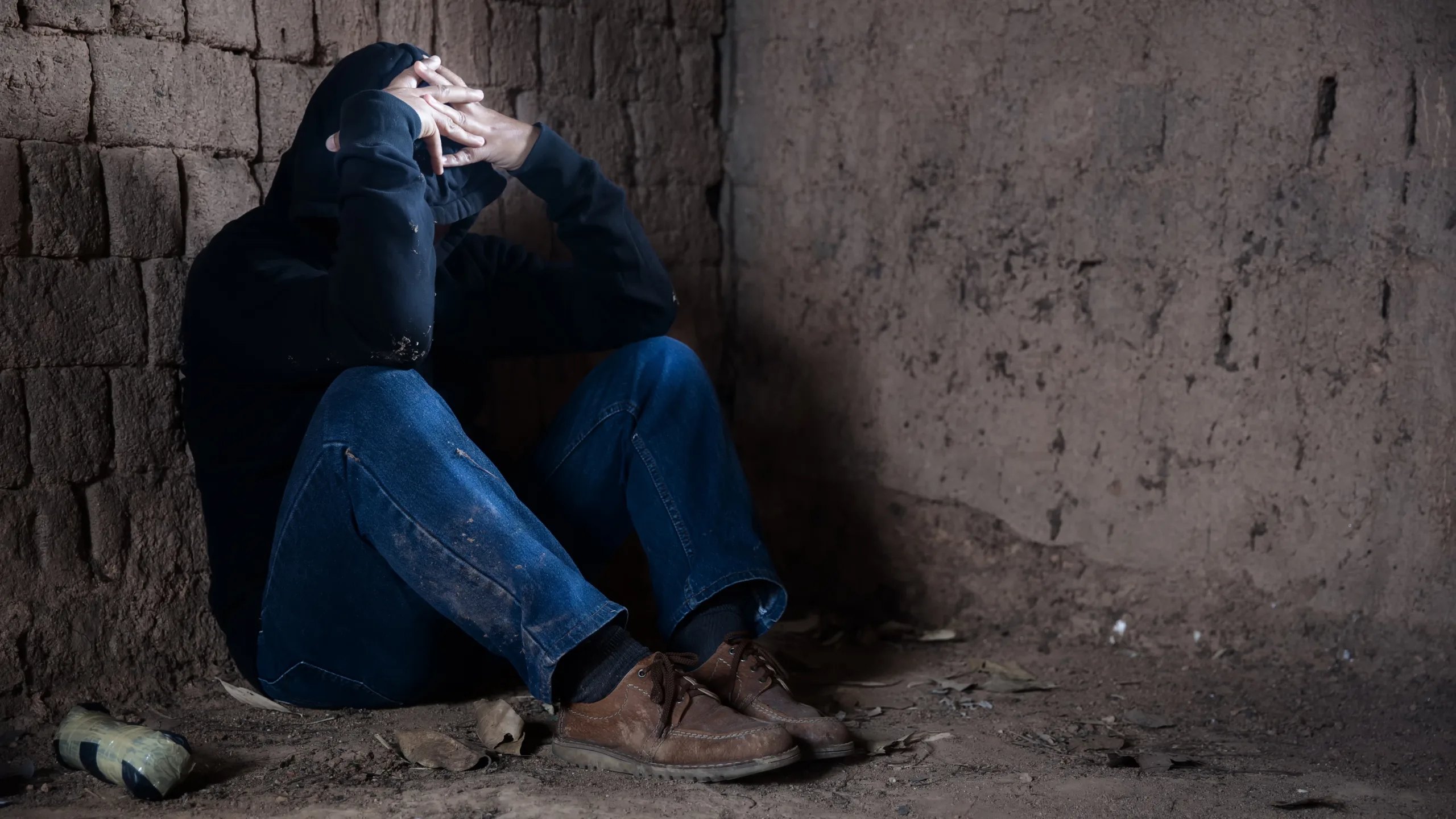 Drugs addiction and withdrawal symptoms concept. Depressed and hopeless man sitting alone after using drugs and drunk alcohol at abandoned house. International Day against Drug Abuse.