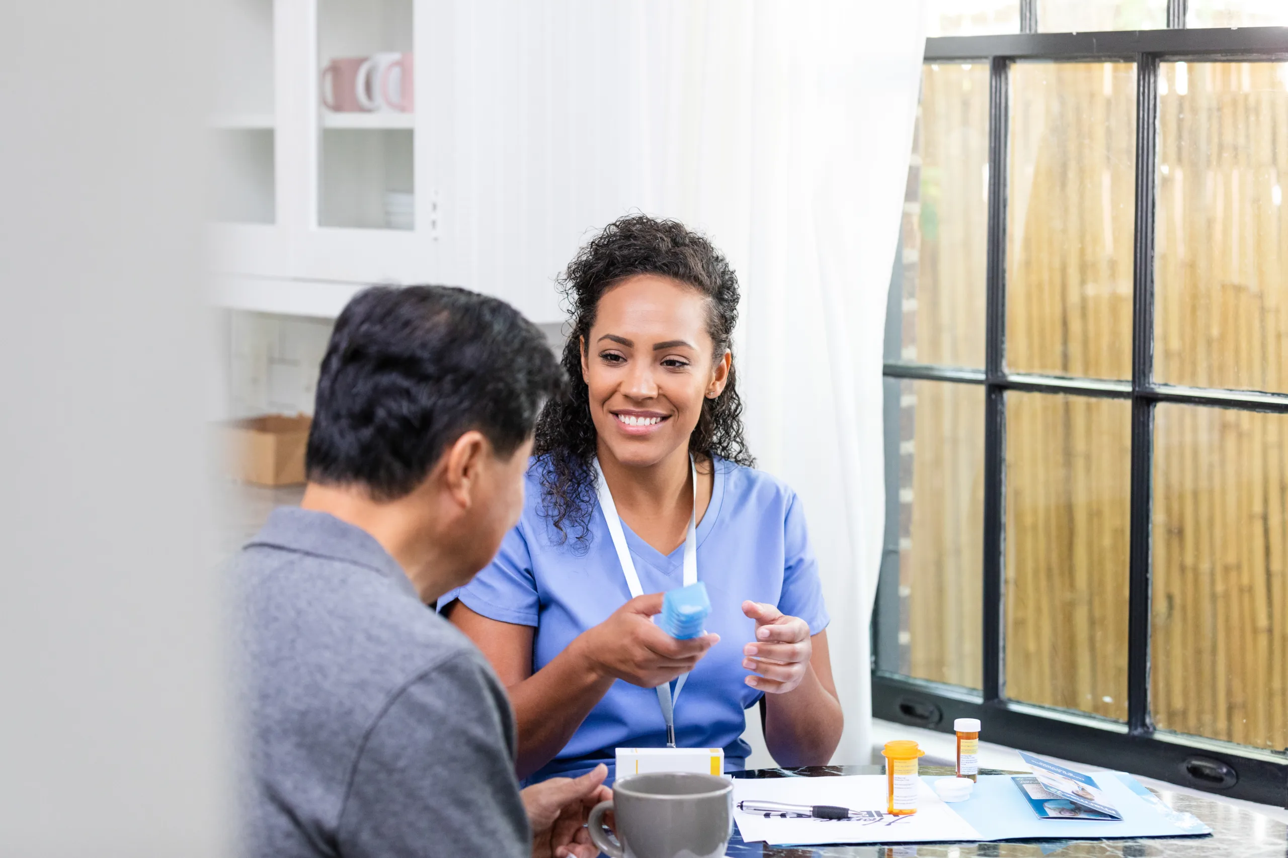 Mid adult nurse uses a pill organizer to sort out a senior male patient's medication.