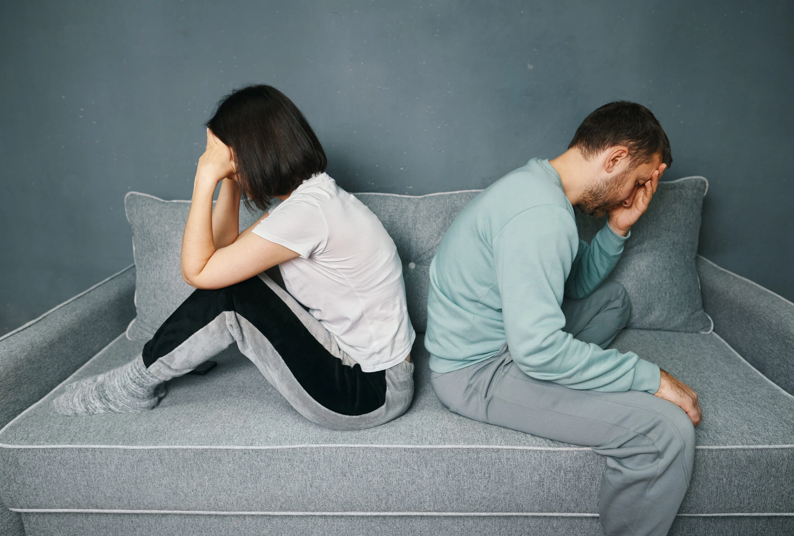 Young couple sitting back to back on the couch and looking offended while having a quarrel. Relationships problems, disagreement, conflicts in marriage, divorced concept
