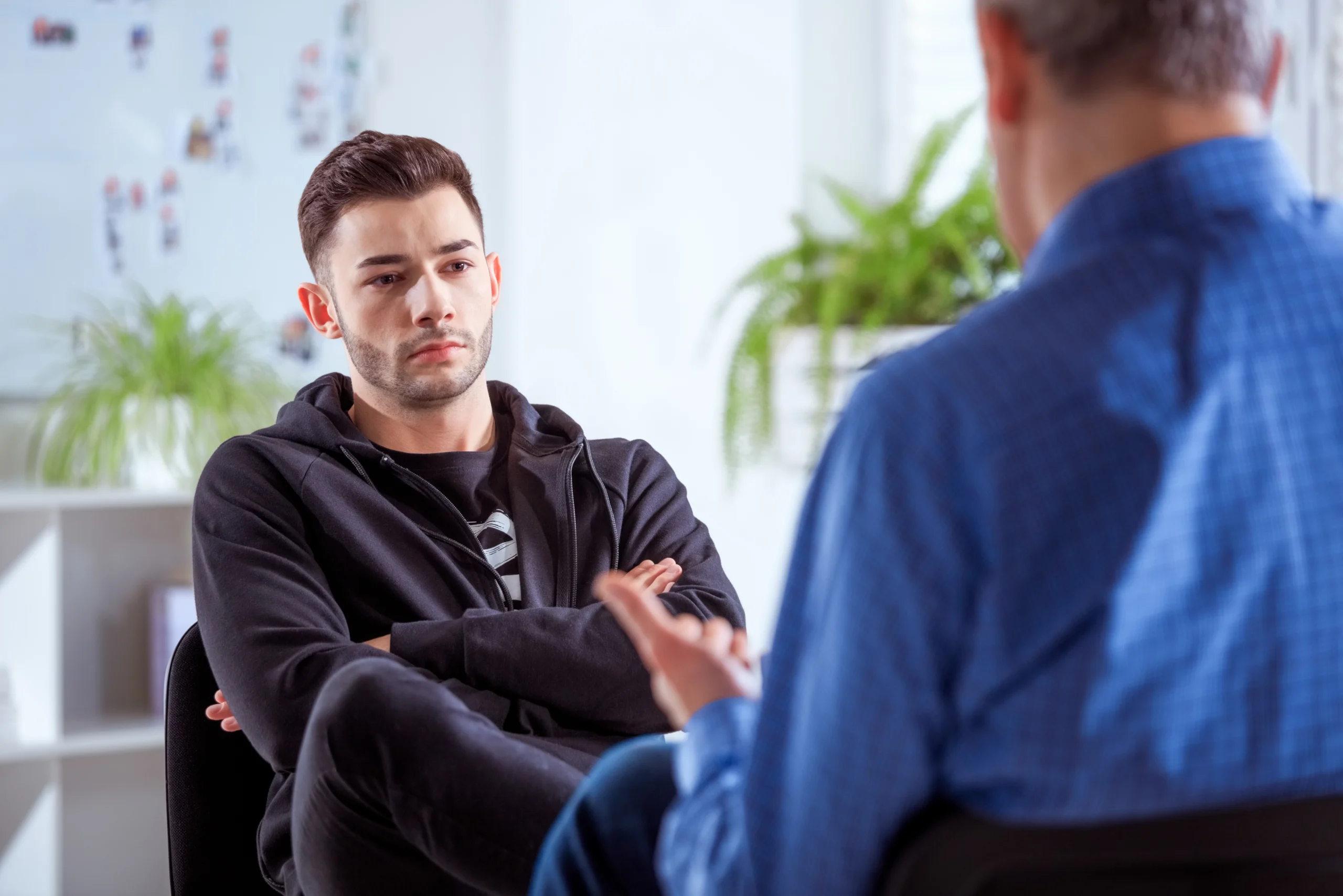 Serious student listening to therapist. Mature professional advising young man during session. They are sitting in meeting at lecture hall.