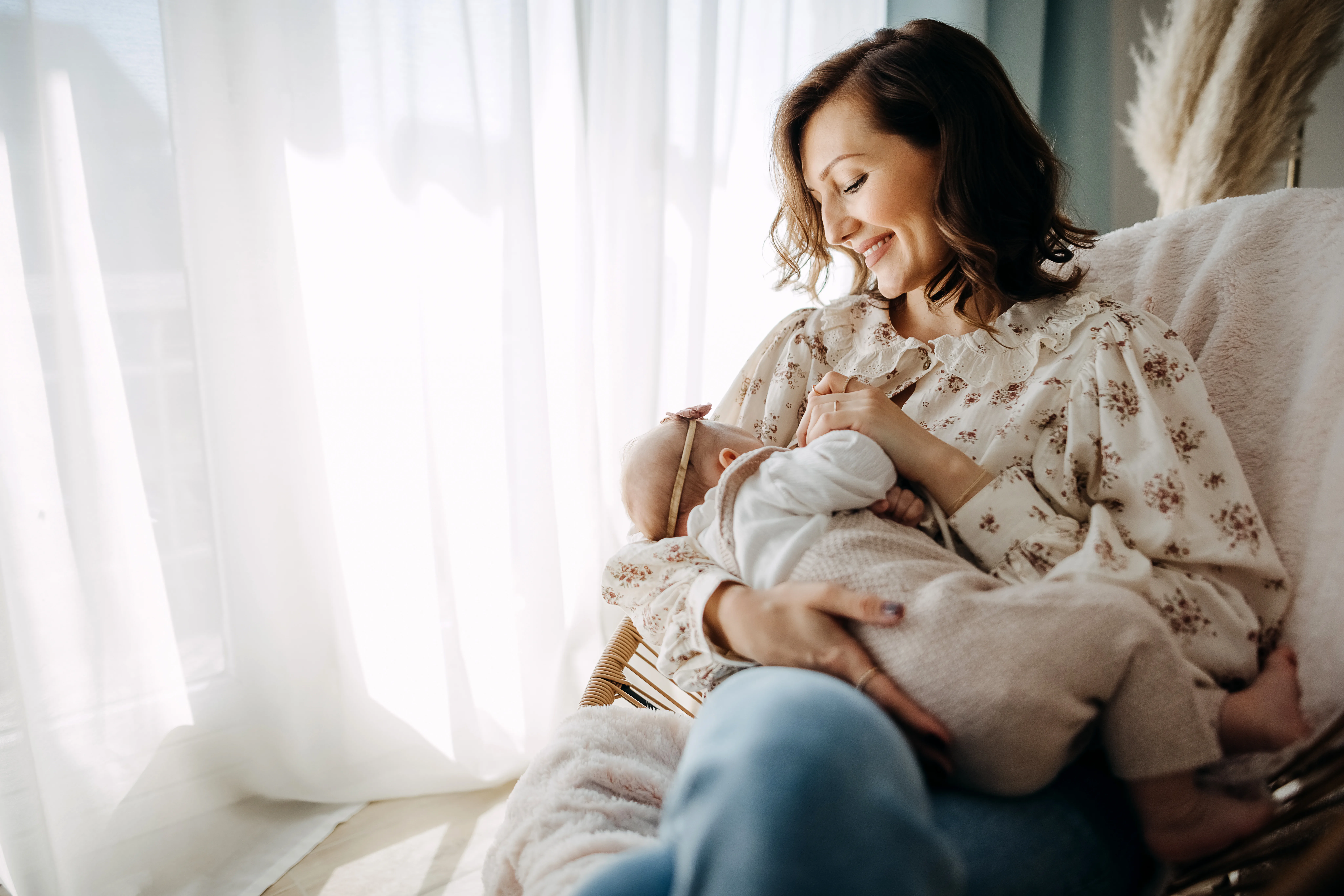 Mother breastfeeding a newborn baby, seating on rocking chair at room.