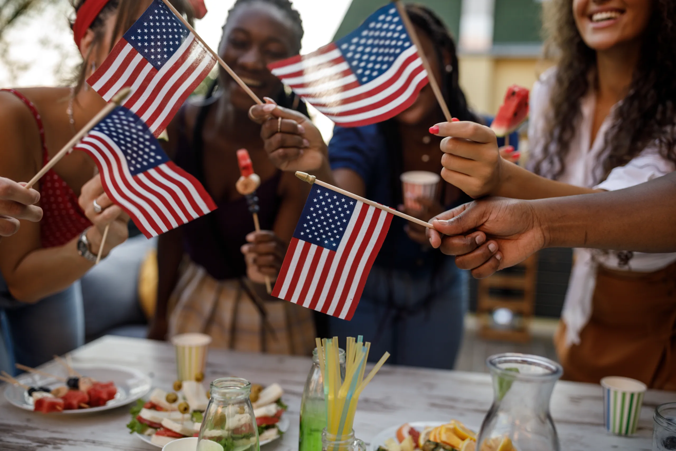 Candid shot of diverse group of joyful young people, friends, having fun, dancing and waving American flags while celebrating 4th of July on the balcony.